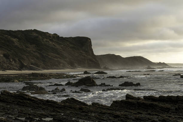 Moody sky with dramatic cloud formations over Carriagem Beach, Portugal. Rugged coastline and rock formations create a striking and atmospheric scene at dusk.