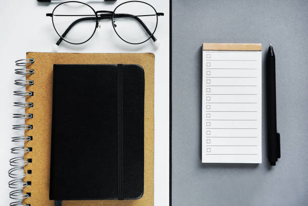 Notepad with to-do list next to notepads, pen, glasses on gray background