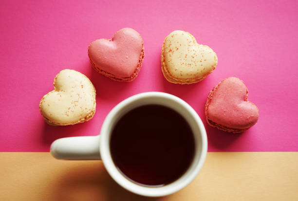 Heart-shaped macarons next to a cup of tea on a pink and yellow background