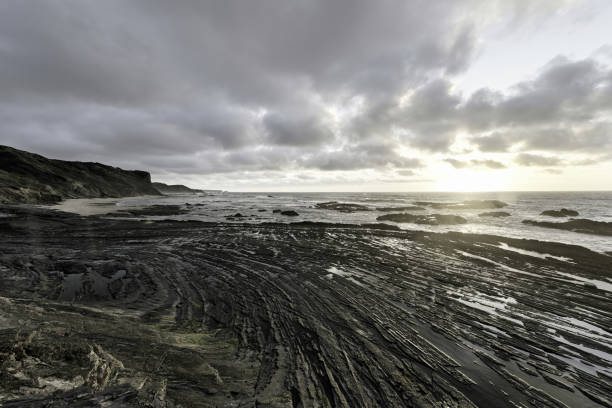 Dramatic clouds and rocky shoreline at Praia da Corriagem, Portugal, captured during sunset.