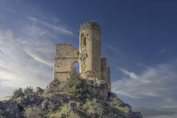 Hayedo de la Tejera negra, Spain - April 30, 2011: Ancient stone castle structure with battlements and towers standing proudly on a green grassy hill under a dramatic cloudy sky, reflecting history and architectural heritage