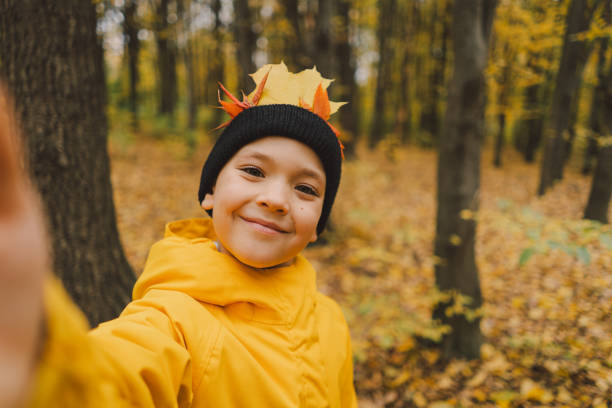 A joyful child dressed in a bright yellow raincoat walks along a serene forest path covered with vibrant autumn leaves. Autumn mood. Beautiful autumn