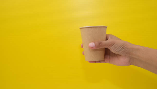 istock Brown paper cup in hand, isolated on yellow background 2165455568