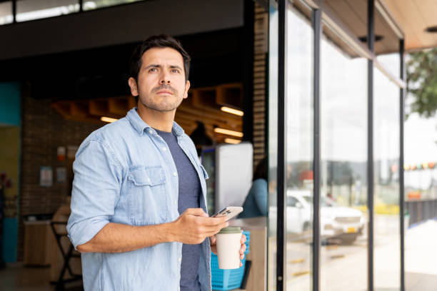 Man leaving a convenience store using his phone and drinking coffee