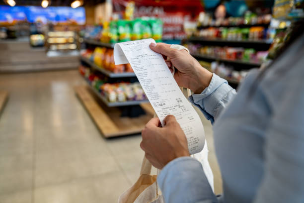 woman shopping at a convenience store and checking her receipt - economie fotos stockfoto's en -beelden