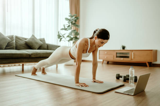 istock Young Asian woman in sportswear doing plank on training mat while watching online workout tutorials on laptop in the living room. Sport and recreation concept 2165463000