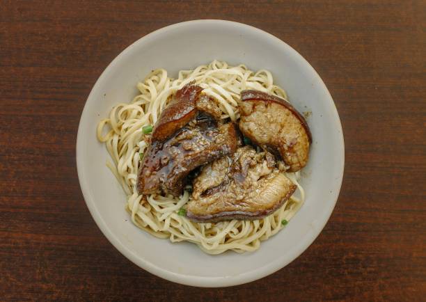 A bowl of Chinese Noodles topped with soy sauce pork belly on a wooden table. Flat lay, overhead, or top view angle.