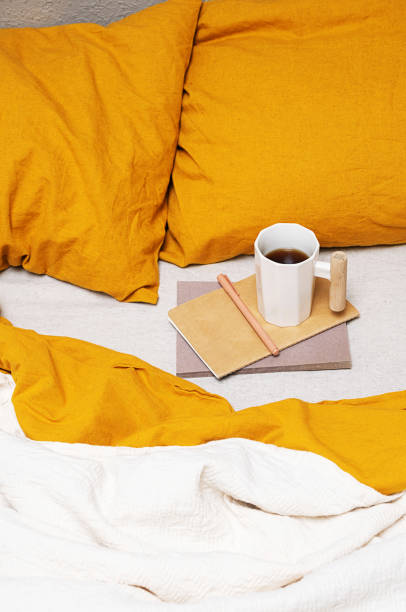 istock Cozy bed with yellow pillows, notebook, pen and coffee mug. 2165473446