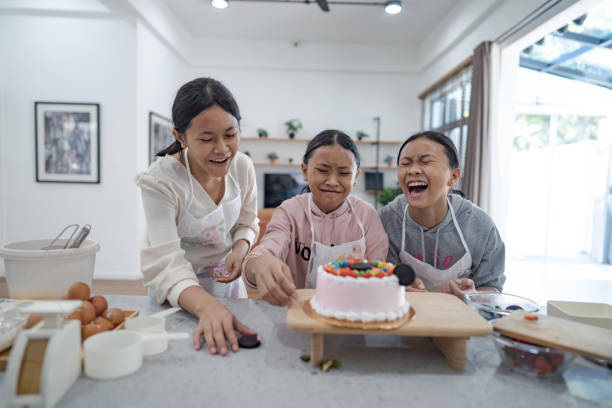 istock Three young girls having fun and laughing while decorating a cake in a home kitchen 2165474845