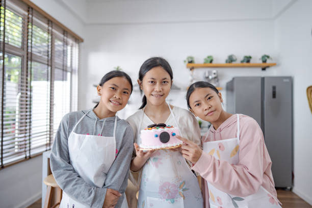 istock Three young girls proudly presenting a homemade cake in a kitchen while wearing aprons 2165474895