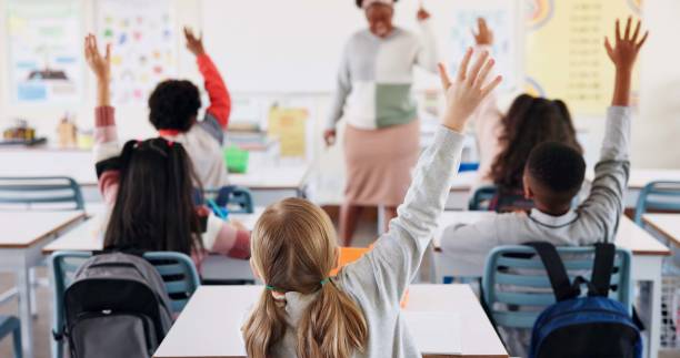 istock Students, classroom and kids with education, questions and knowledge with book, practice and thinking. Answer, school and smart with intelligent, learning and teacher with assignment and children 2165474976