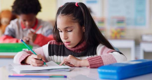istock Students, classroom and girl with education, writing and knowledge with book, practice and pencil. Kids, school and smart with intelligent, learning and exam with assignment, project and creativity 2165476230