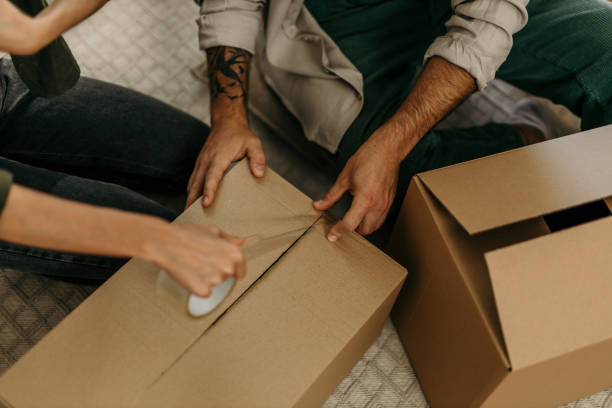 Happy young Caucasian couple moving out of their old apartment. Close up on a hands packing cardboard box