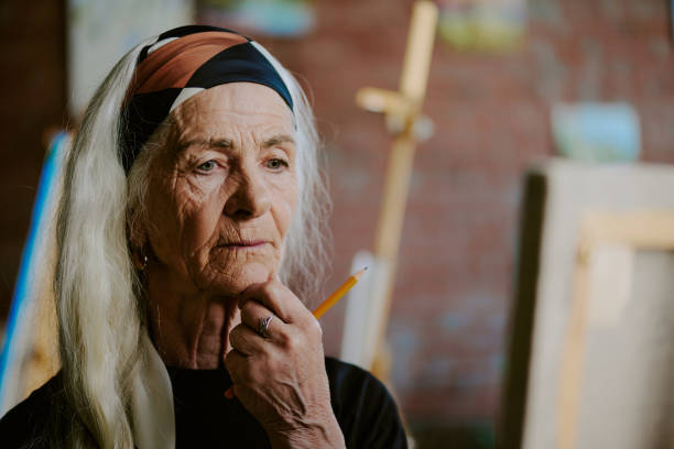 Senior woman enjoying creative hobby painting on canvas wearing headphones