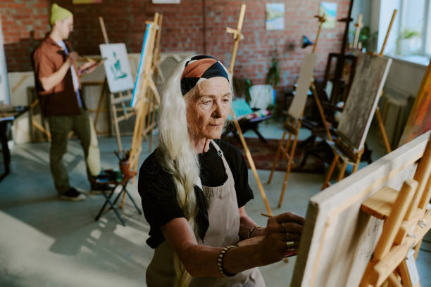 High angle view senior Caucasian woman with long hair attending art class painting on canvas