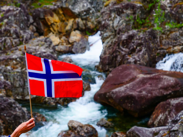 Tourist hand holding norwegian flag outdoor against rocks mountain nature