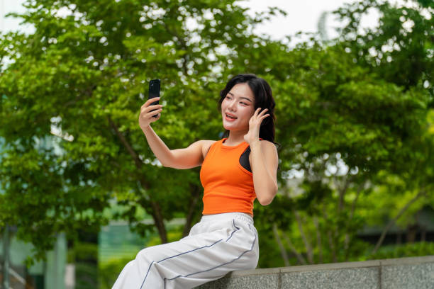istock Young Woman Using Phone Taking a Selfie in A Park 2165482987