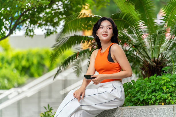 istock Young Woman Using Phone in Park Looking Away Contented 2165483302