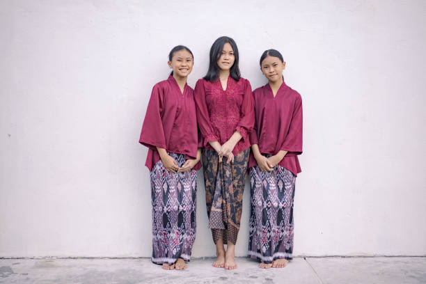 Three sisters standing together against a plain background, wearing traditional maroon attire and patterned skirts, posing for a photograph