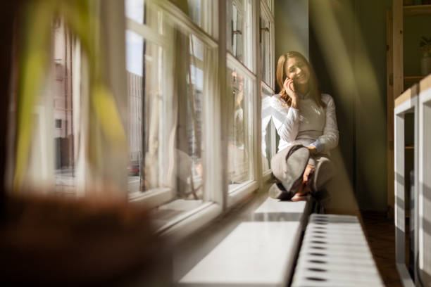 Businesswoman Relaxing on Window Ledge with Smart Phone