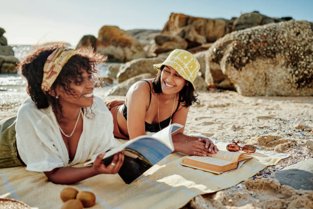 istock Laughing young friends reading while relaxing on a beach in summer 2165496577