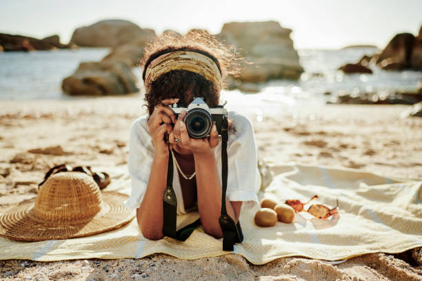 istock Young woman taking photos while relaxing on a sandy beach 2165496802