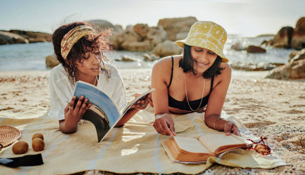 Smiling young friends reading during a beach day in summer