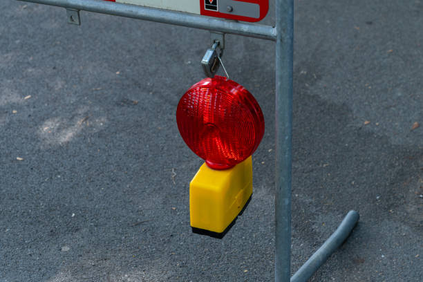 A red warning light hangs from a metal frame at a construction site, alerting pedestrians and drivers to safety hazards nearby.