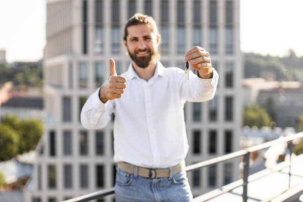 istock Man smiling with keys and thumbs up on rooftop 2165512609