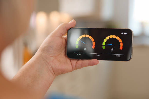 istock Person Holding Smartphone Displaying Energy Consumption Meter in Bright Indoor Environment During Daytime 2165516282