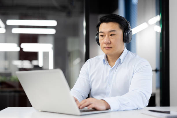 istock Focused Asian professional working with laptop and headphones 2165517016