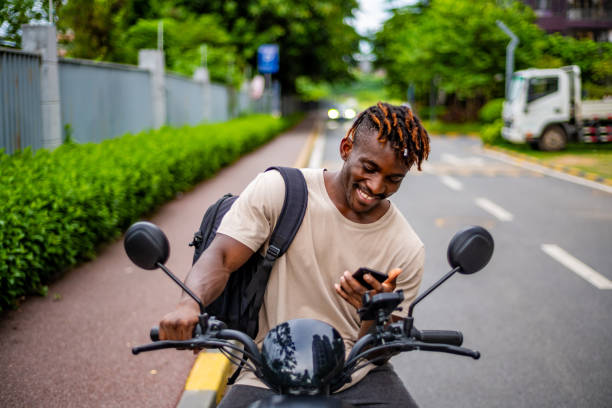 istock Joyful Black Man Using Smartphone on Motorbike 2165519251