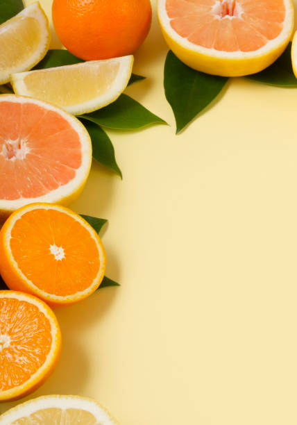 Tropical fruits, lemon, orange, grape fruits and green leaves on soft yellow paper background