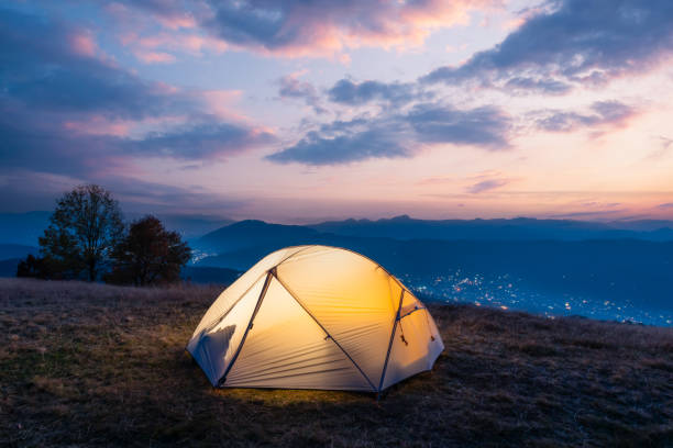 Tourists tent lighted from the inside by a warm light against the backdrop of an incredible mountains landscape during sunset