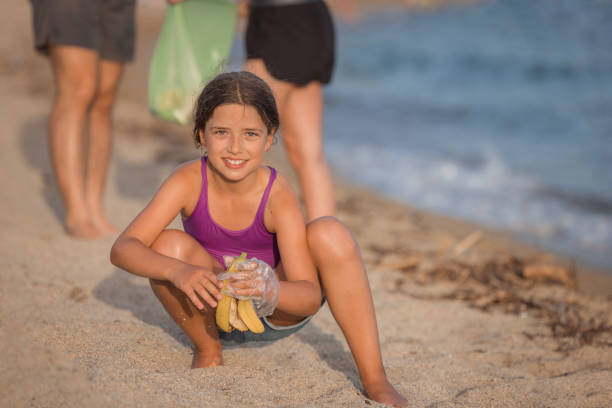 Young girl wearing plastic gloves when holding an old banana peel and cleaning the beach