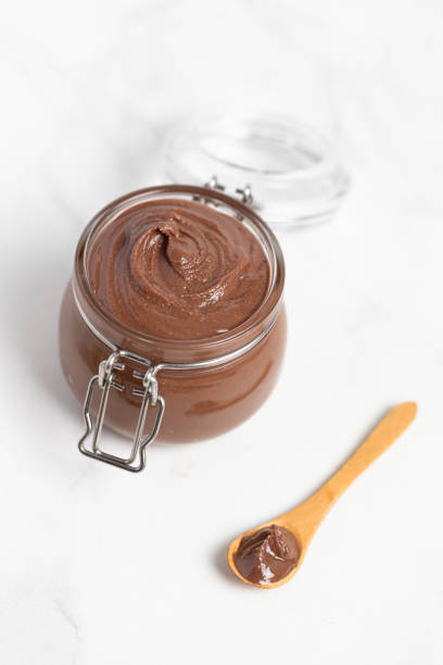 istock Chocolate butter, chocolate-nut paste in a glass jar on a light table, wooden spoon 2165524292