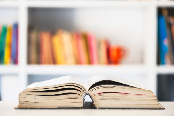 istock Opened book with blurred shelfbook of library 2165526283