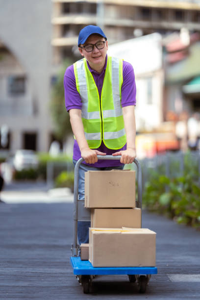 Close up of a delivery woman holding in one hand smartphone for signature from home delivery customer and in the other cardboard box, copy space.
