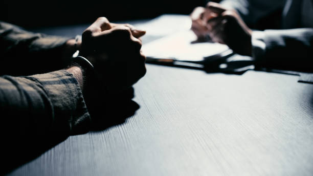 istock Suspected man in handcuffs tightly clasping his hands together while talking to a detective 2165533460