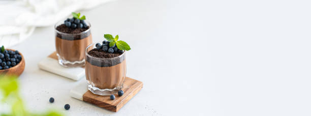 istock Vegan chocolate mousse dessert banner. Chocolate pudding in glasses decorated with fresh blueberry and mint on a white concrete background. Copy space. Confectionery web line 2165536815