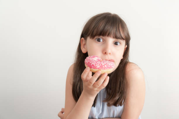 istock Little girl is eating pink doughnut 2165540595