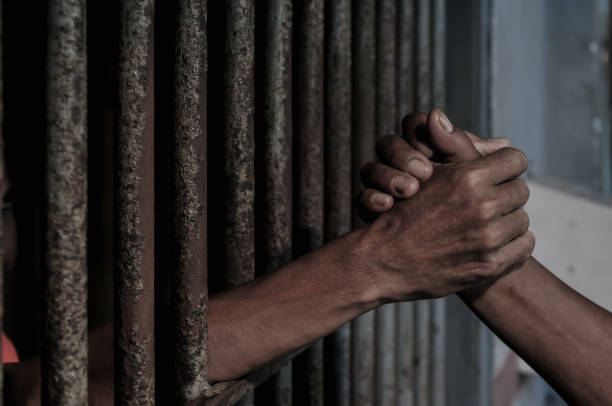 istock hands of a prisoner behind prison bars on black background 2165543719