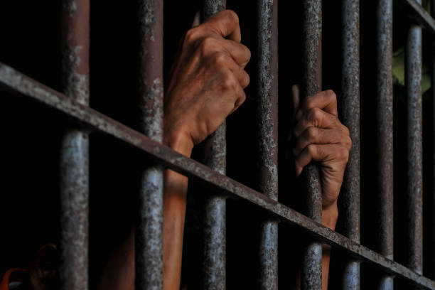 istock hands of a prisoner behind prison bars on black background 2165543825