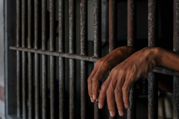 istock hands of a prisoner behind prison bars on black background 2165543855