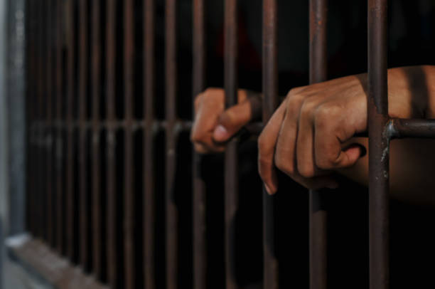 istock hands of a prisoner behind prison bars on black background 2165543891