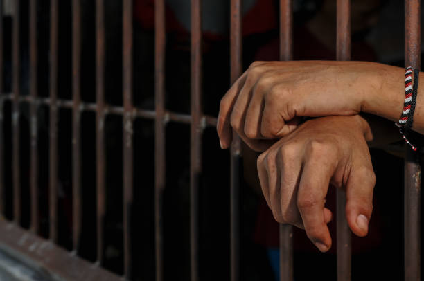 istock hands of a prisoner behind prison bars on black background 2165543918