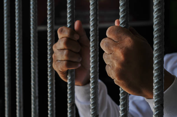 istock hands of a prisoner behind prison bars on black background 2165543922