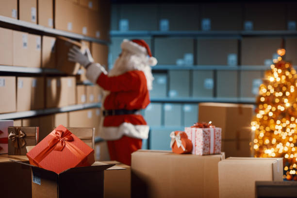 Santa Claus working in the warehouse, he is preparing delivery boxes filled with Christmas gifts