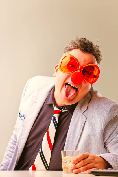 istock Businessman wearing clown costume drinking at work 2165550792