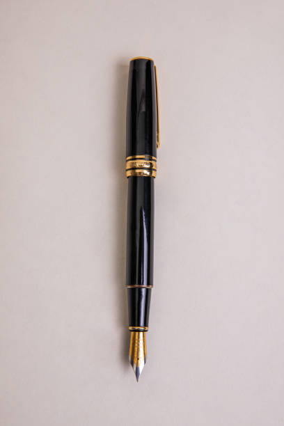 elegant black metal fountain pen with gold details in overhead view on beige background